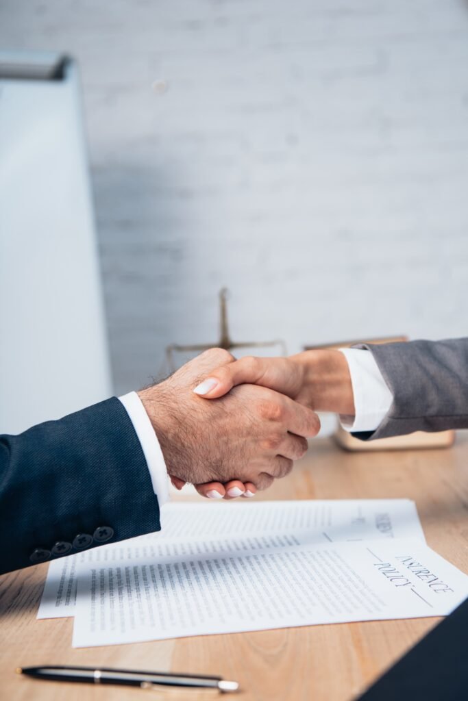 cropped view of businessman and businesswoman shaking hands near insurance policy documents